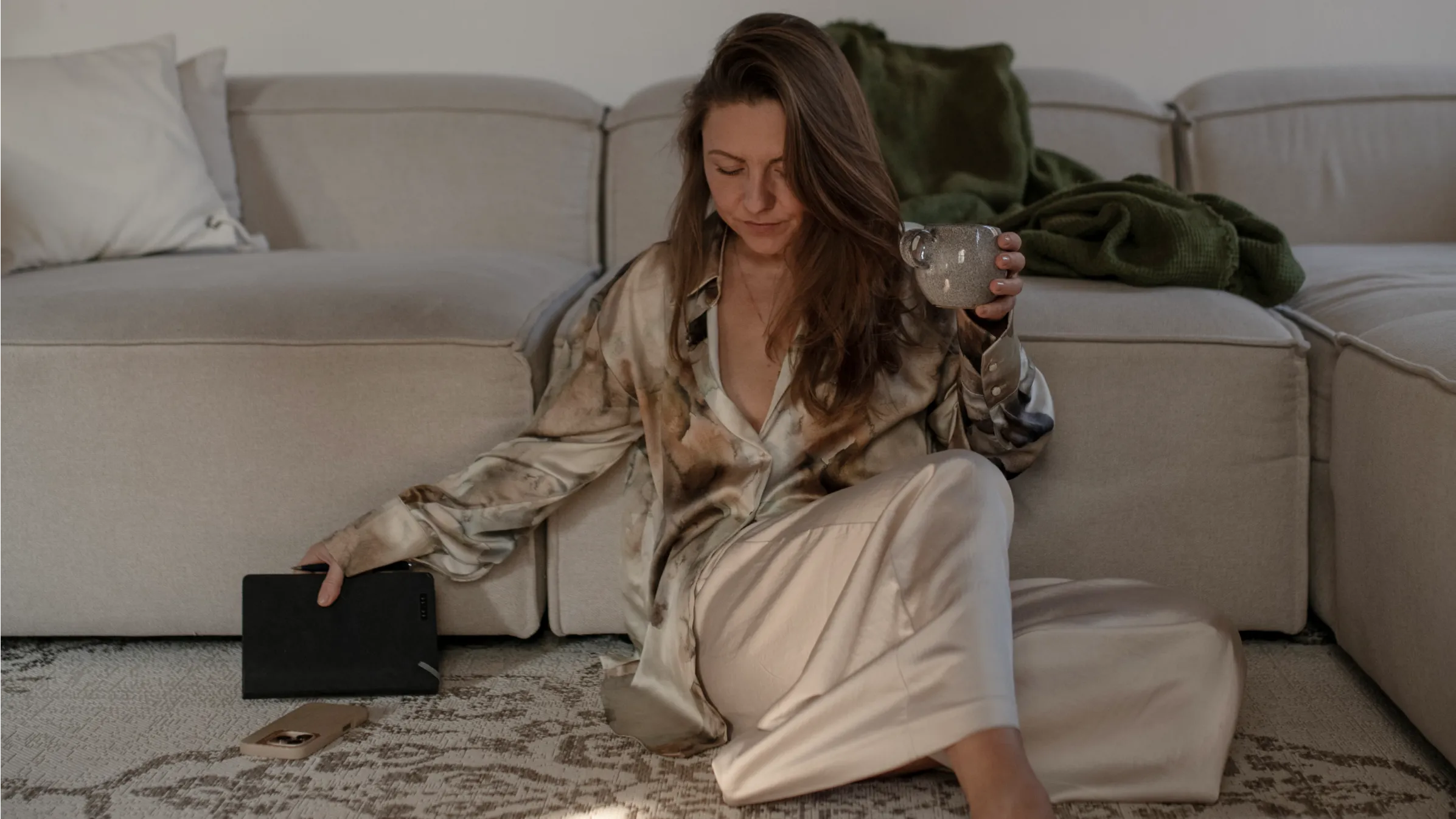 Yavi Hameister sitzt entspannt vor dem Sofa mit Tasse in der Hand - Coachin für zyklisches Leben